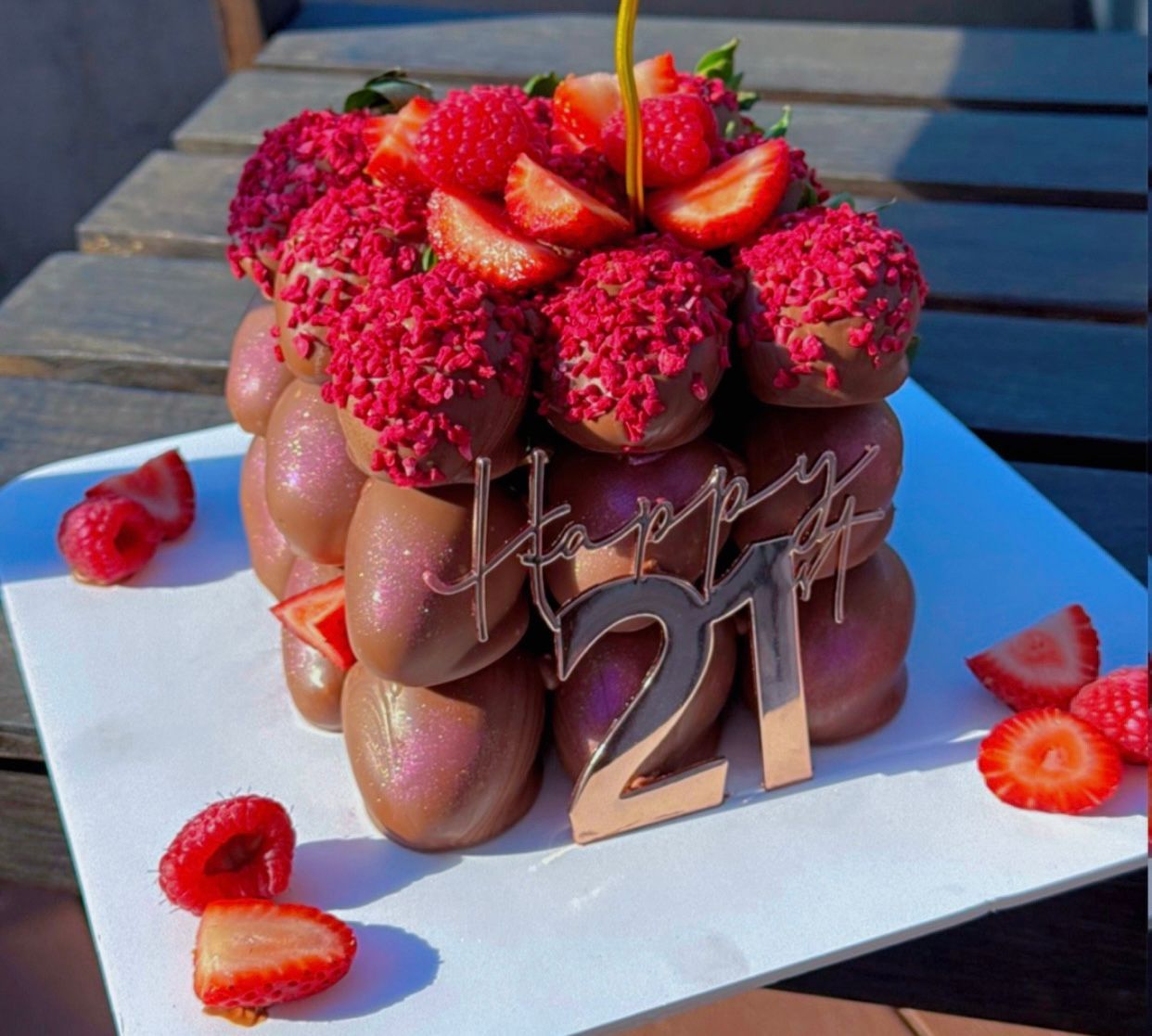 Cake decorated with strawberries, blueberries, chocolate hearts, and pink frosting drips on a wooden cake stand.