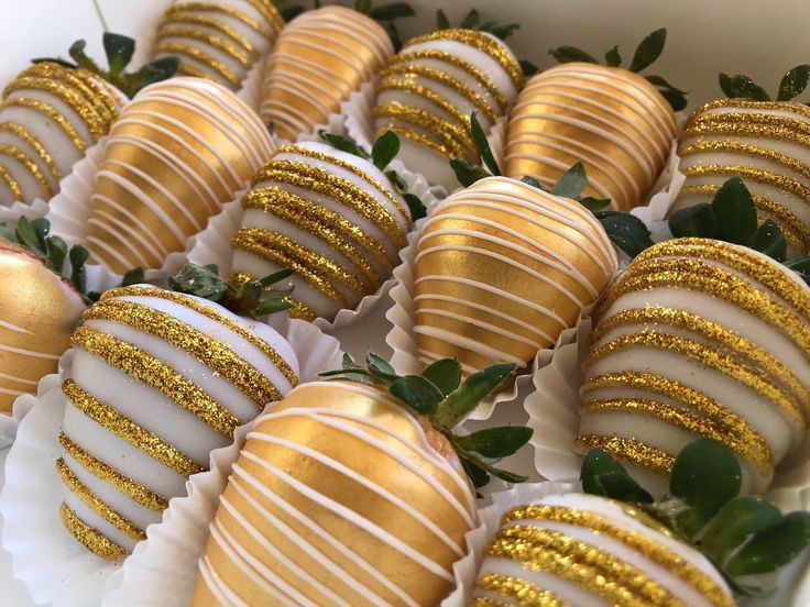 A close-up view of chocolate-covered strawberries decorated with alternating gold glitter and white icing stripes.
