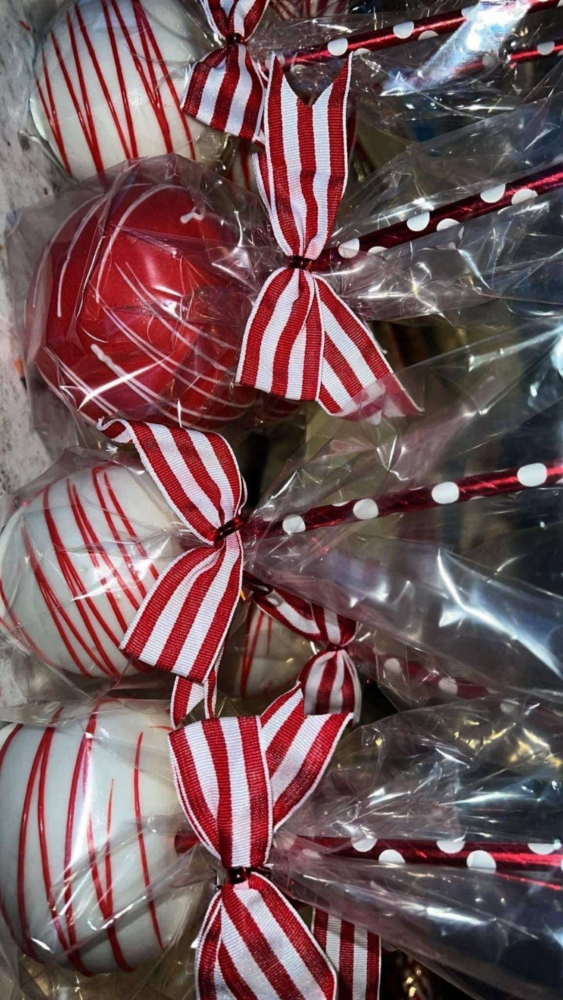 Cake pops decorated in red and white stripes and candy cane themes, wrapped in plastic and tied with red striped bows.