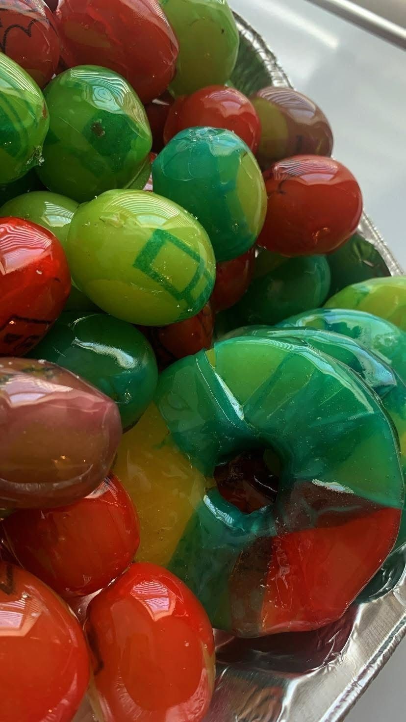 A tray filled with small, colorful, glazed round treats and one larger ring-shaped dessert in green, red, and yellow.