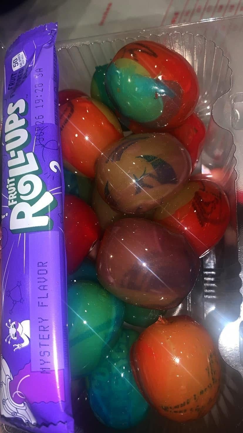 A package of Fruit Roll-Ups beside a clear plastic container filled with various brightly colored, dyed hard-boiled eggs.