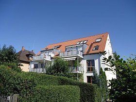 Ein großes weißes Haus mit einem roten Ziegeldach ist von Bäumen und Büschen umgeben.