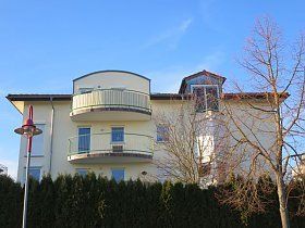 Ein großes weißes Haus mit einem Balkon und einem Zaun davor.