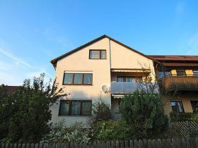 Ein großes Haus mit einem Zaun darum und einem blauen Himmel im Hintergrund.