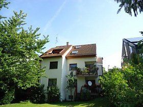 Ein weißes Haus mit braunem Dach ist von Bäumen und Gras umgeben.