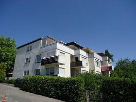 Ein großes weißes Wohnhaus mit Balkonen und einem blauen Himmel im Hintergrund.
