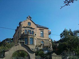 Auf der Spitze eines Hügels steht ein großes Haus, umgeben von Bäumen.