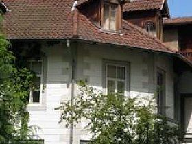 Ein weißes Haus mit einem roten Ziegeldach und vielen Fenstern, umgeben von Bäumen.