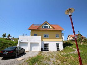 Ein gelb-weißes Haus, vor dem ein schwarzes Auto geparkt ist.