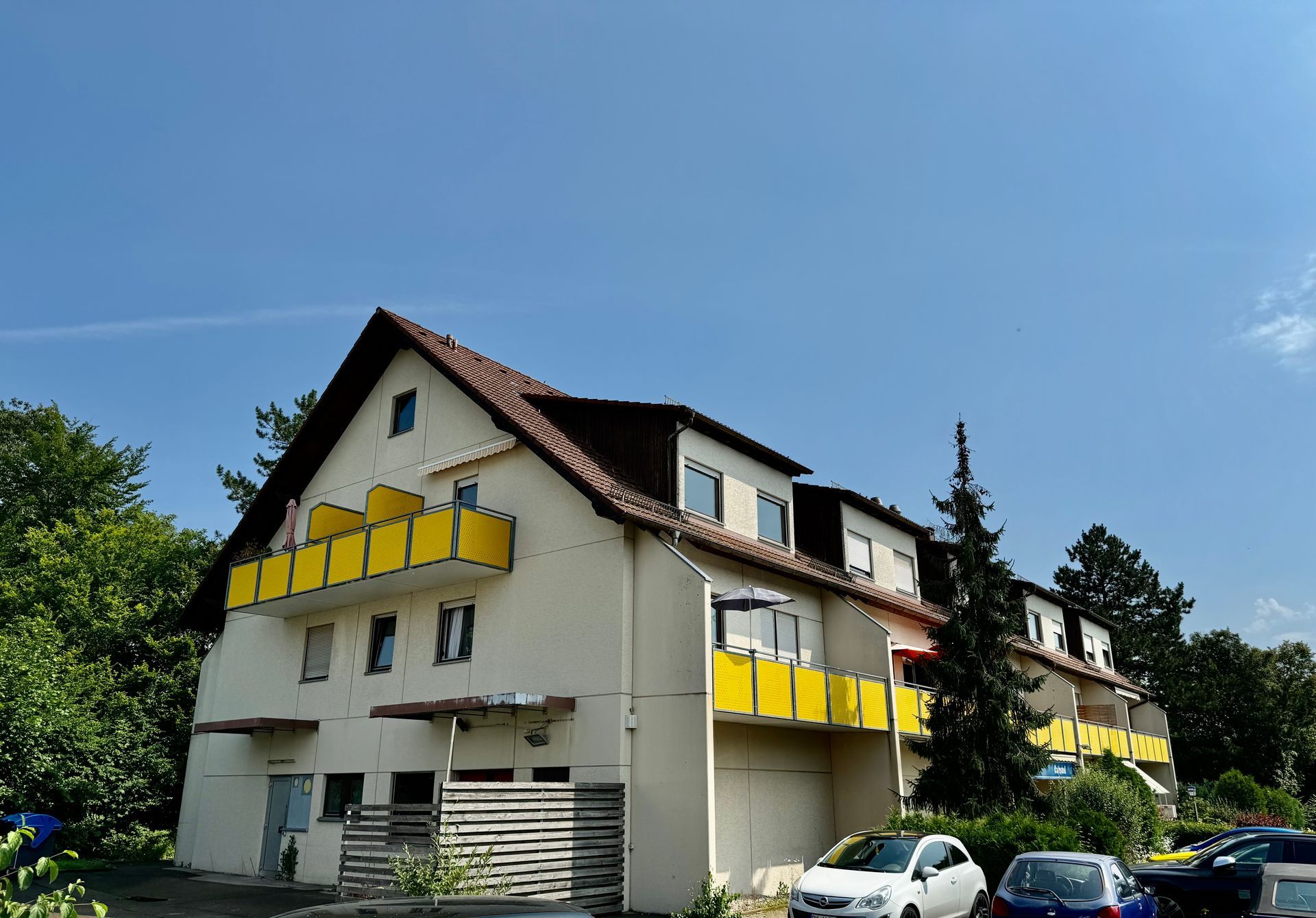 Ein großes weißes Haus mit gelben Balkonen und davor geparkten Autos