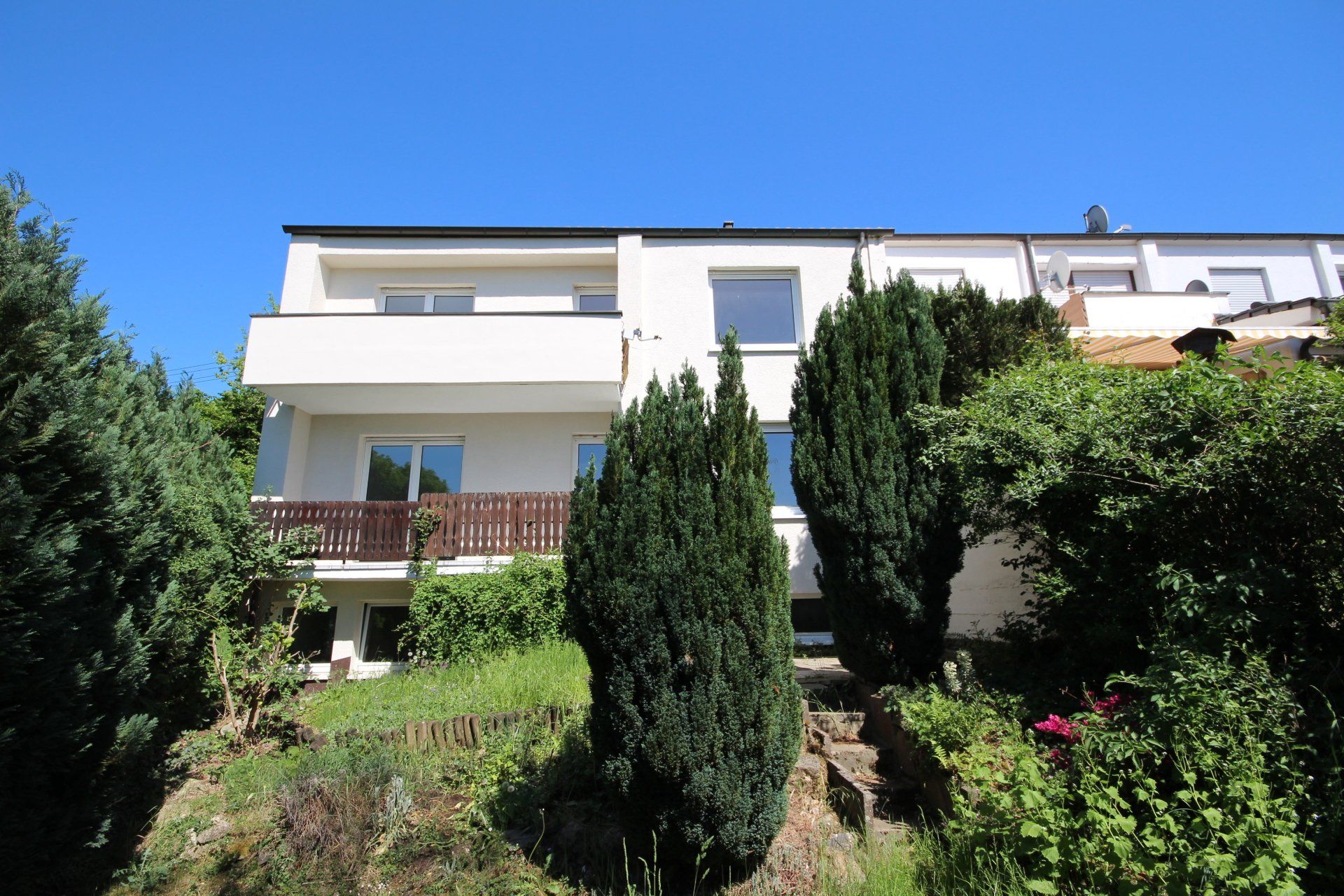 Ein großes weißes Haus mit Balkon ist von Bäumen und Büschen umgeben.