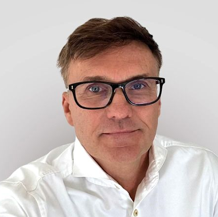 Ein Mann mit Brille und blauem Hemd lächelt in die Kamera.