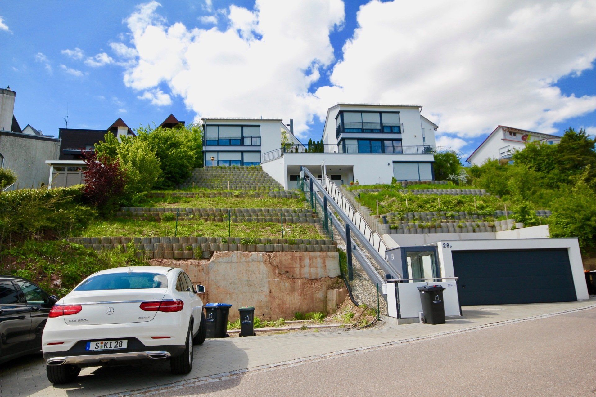Ein weißes Auto parkt vor einem Haus auf einem Hügel.