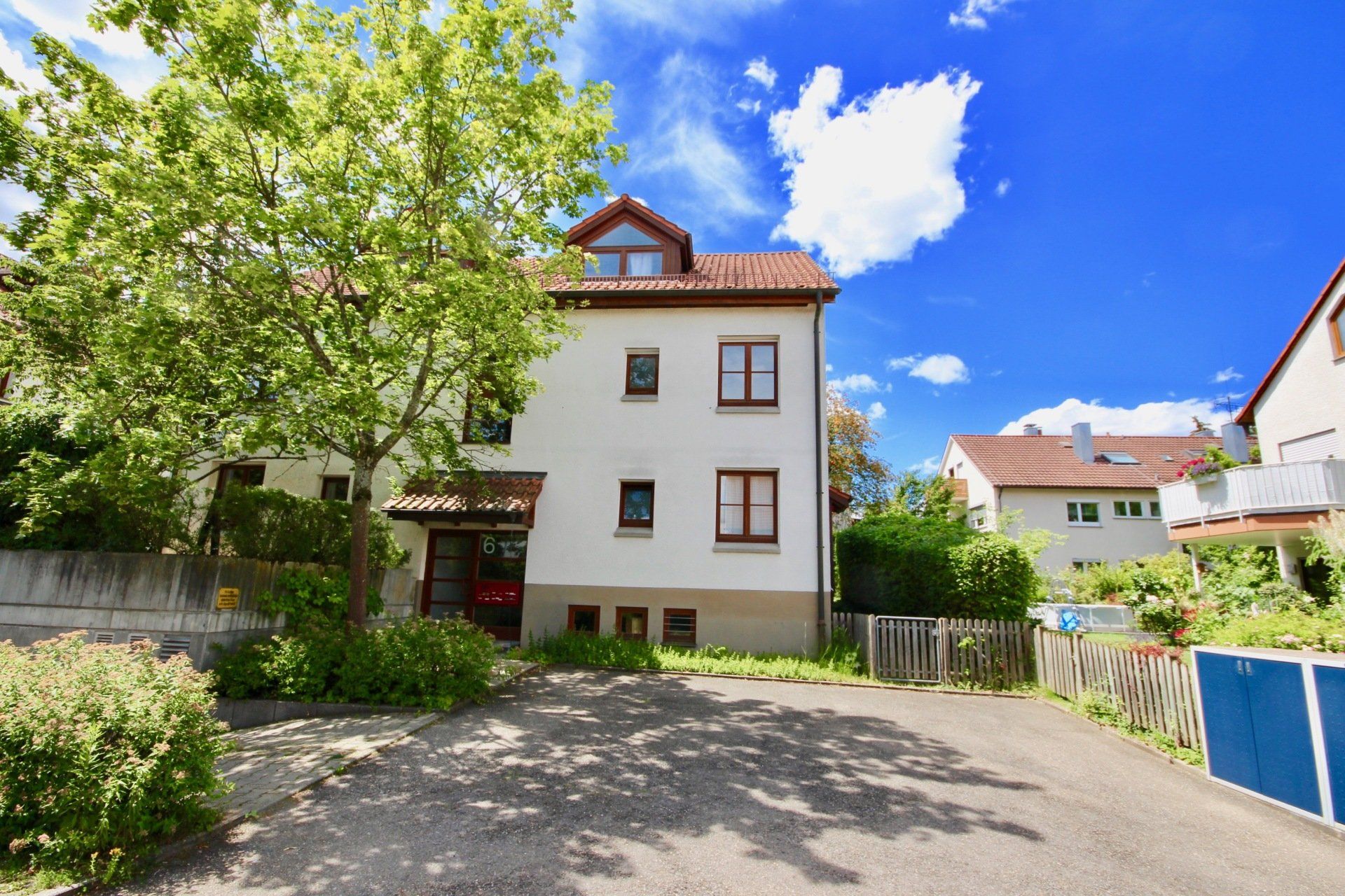 Ein großes weißes Haus mit rotem Dach ist von Bäumen und Büschen umgeben.