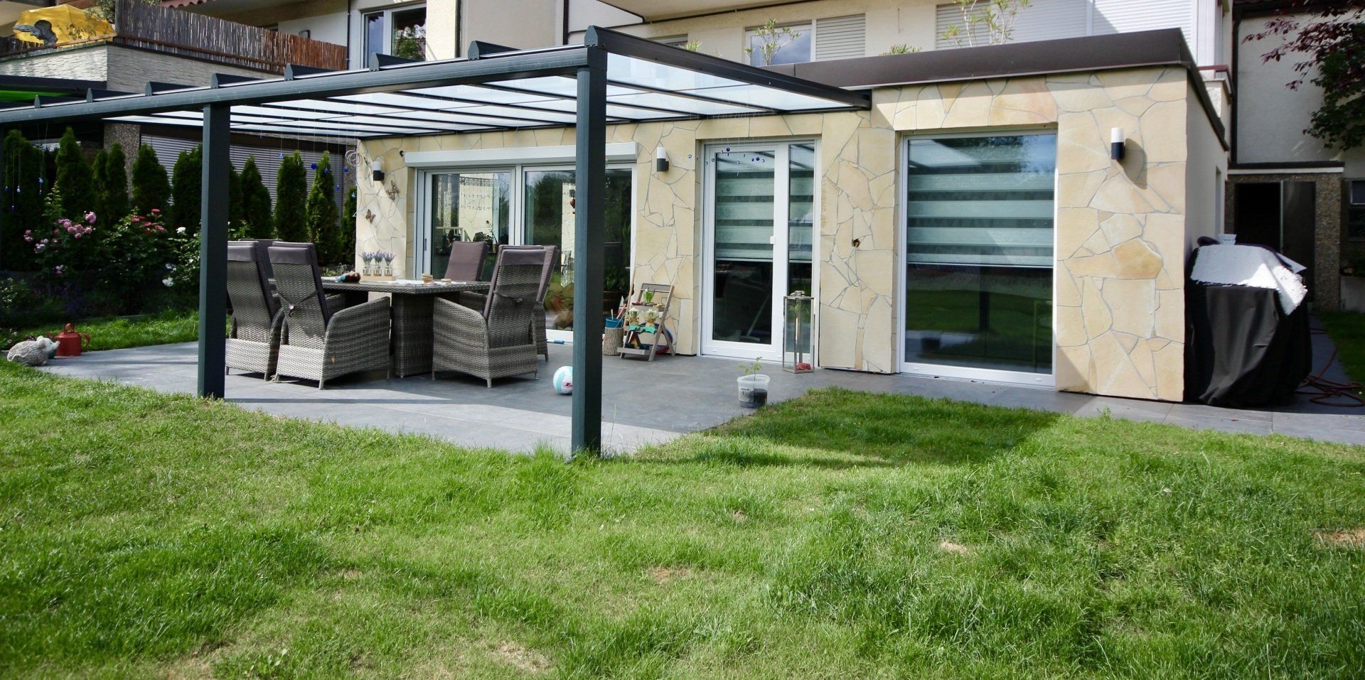 Eine Terrasse mit Pergola und Tisch und Stühlen vor einem Haus.