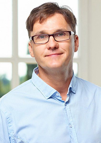 Ein Mann mit Brille und blauem Hemd lächelt in die Kamera.