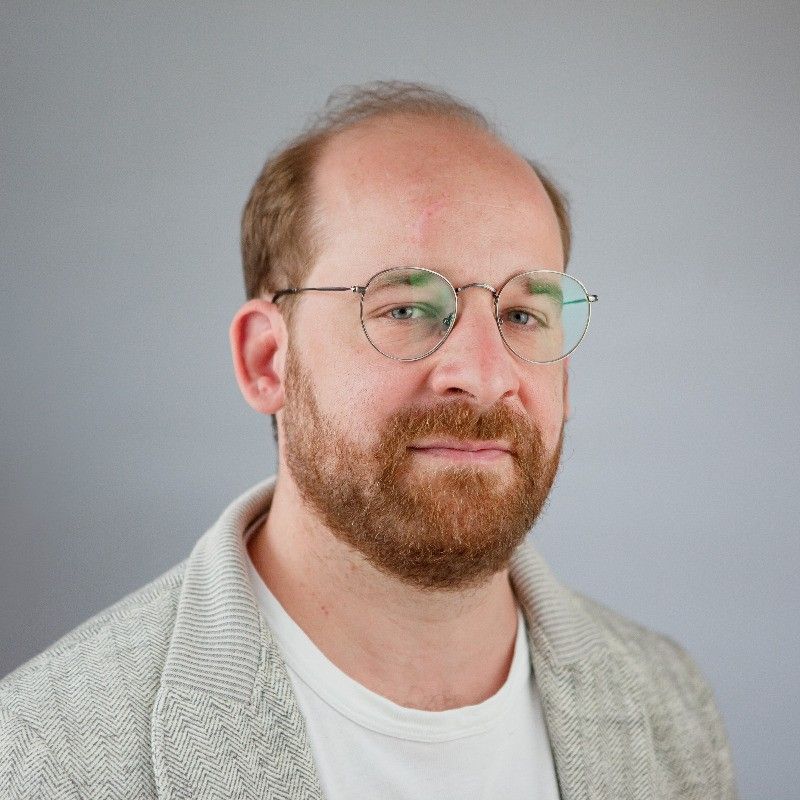 Ein kahlköpfiger Mann mit Bart, Brille und weißem Hemd.