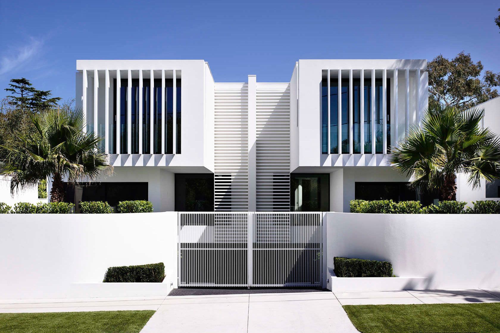 A modern white house with a fence in front of it.