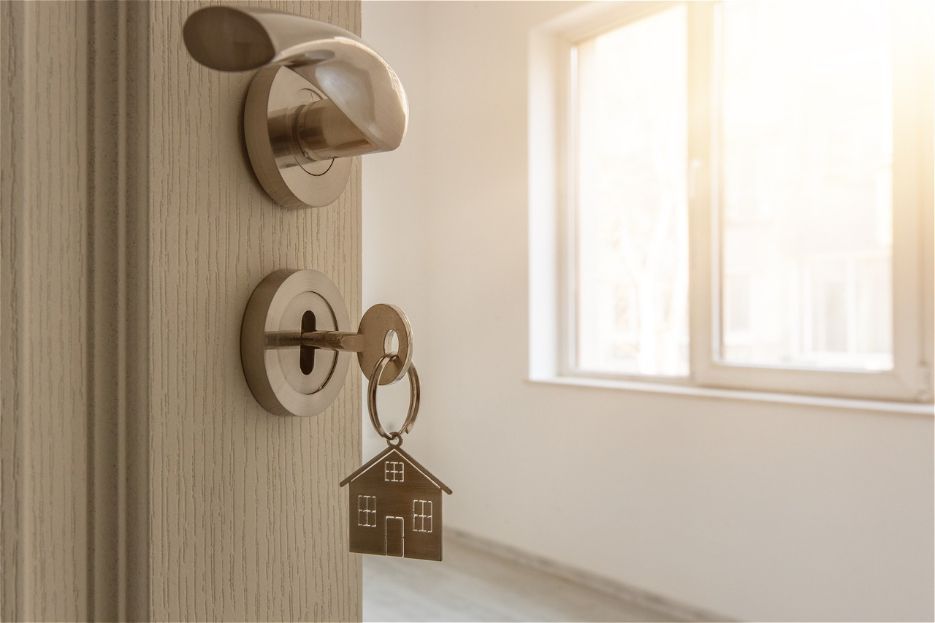 An open door with a key in the lock and a keychain in the shape of a house.