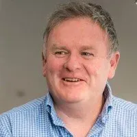 Man with fair skin, smiling, wearing a blue plaid shirt.