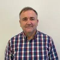 Man in a plaid shirt smiles at the camera against a white background.