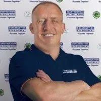 Man in navy blue polo shirt smiling with arms crossed, standing in front of a logo backdrop.