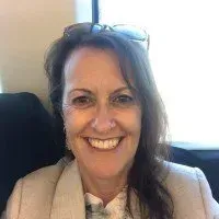 Woman with brown hair, smiling, wearing a light-colored jacket, with glasses on her head.