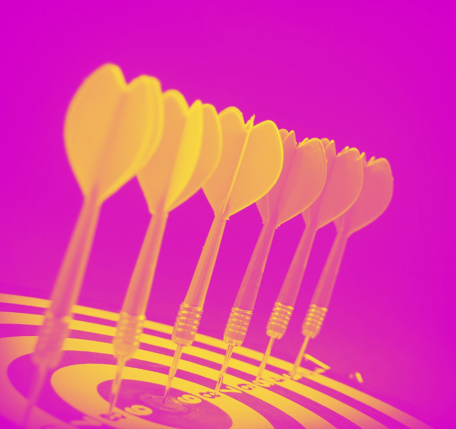 Yellow darts lined up on a dartboard, set against a vibrant magenta background.