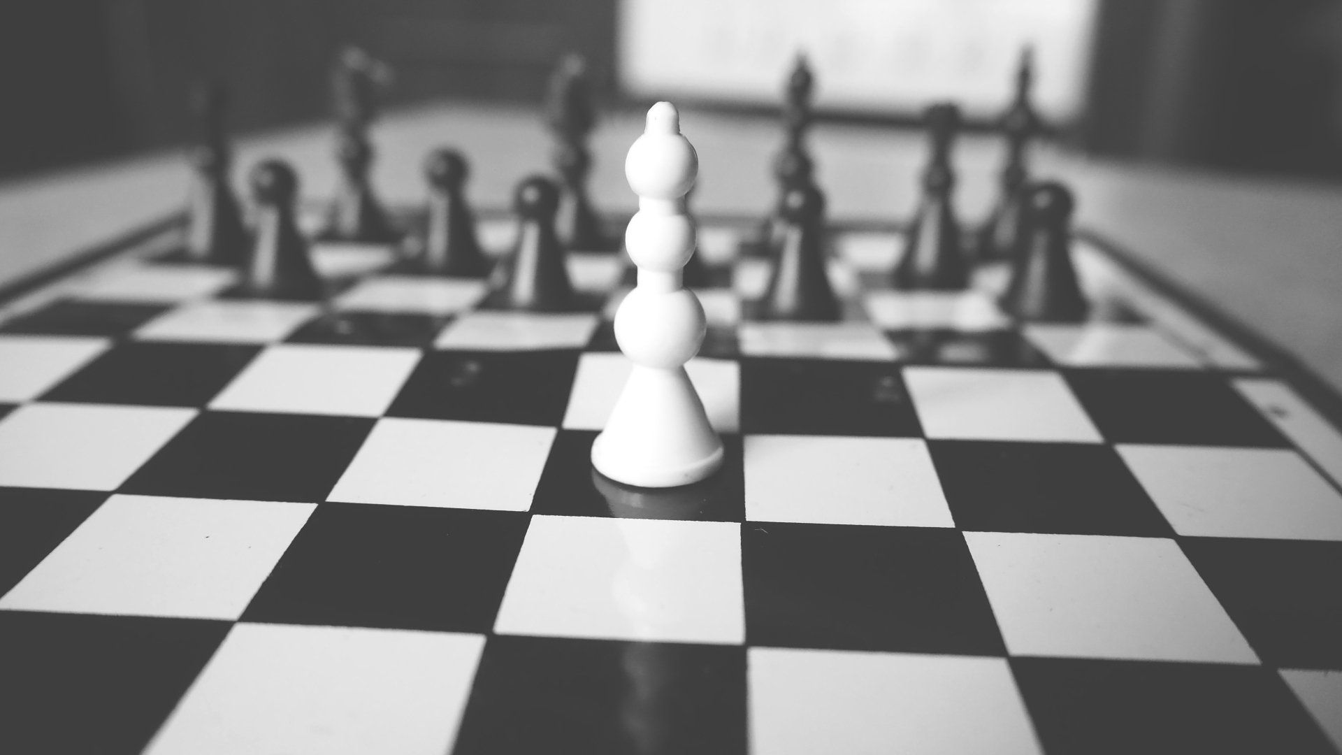 White chess bishop on a chessboard, facing black pieces in the background.