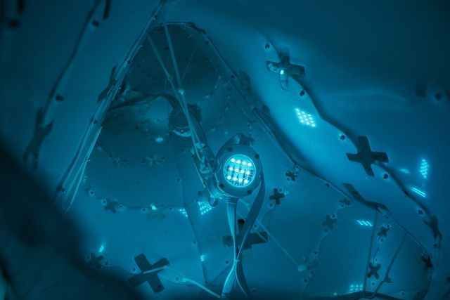 Blue-lit interior with a circular light fixture and abstract shapes resembling wings or crosses.