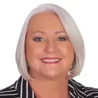 Woman with white hair and a striped blazer smiles at the camera.