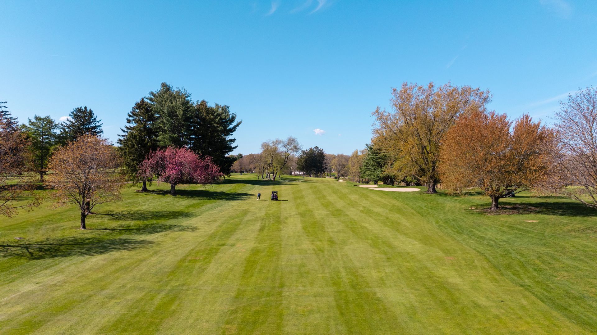 An aerial view of a golf course surrounded by trees on a sunny day.