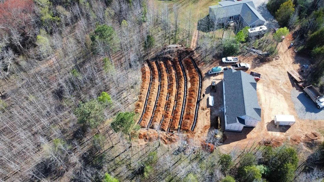 Aerial view of a construction site with a house and long, parallel trenches cut into the dirt.