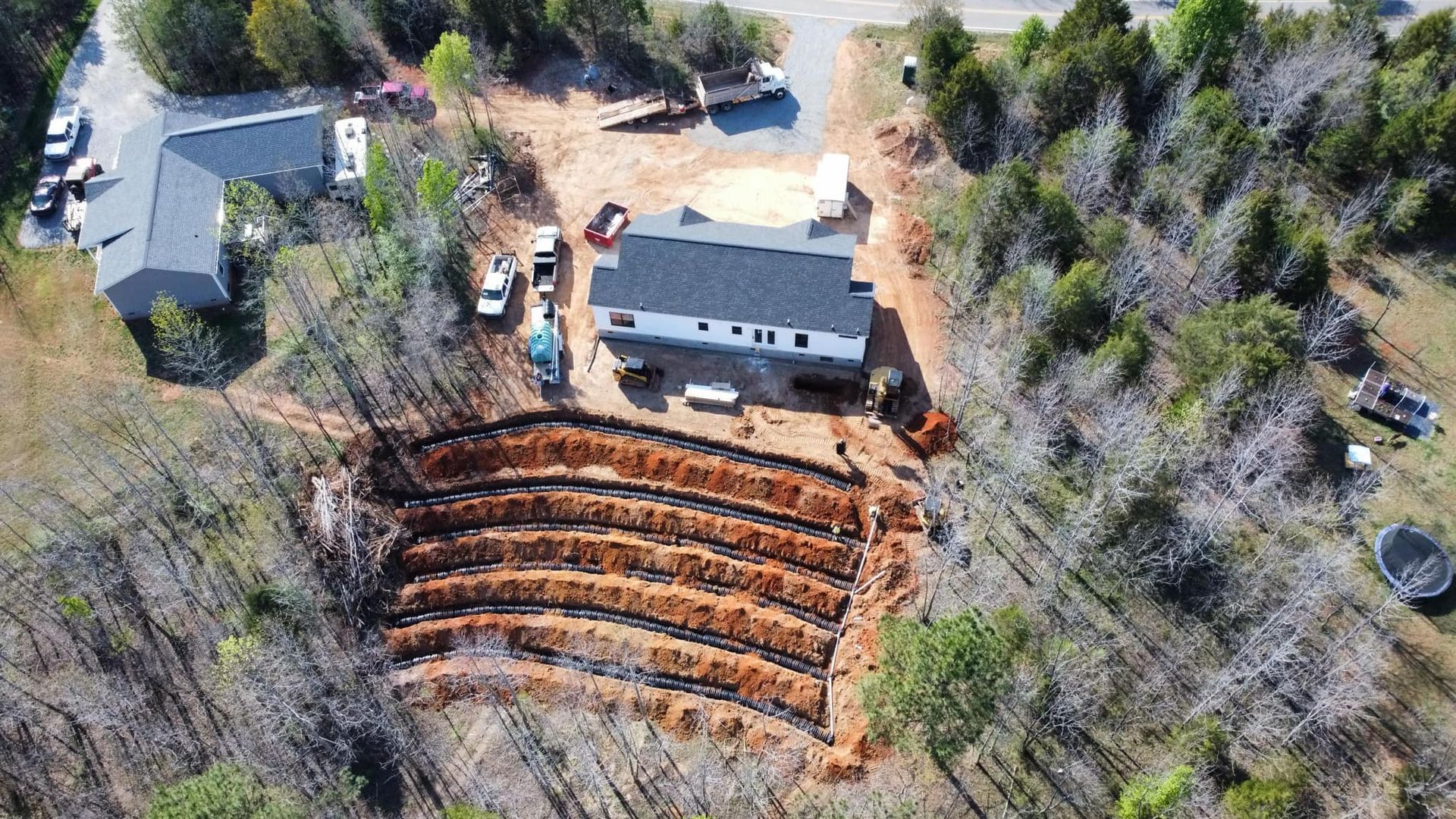Aerial view of a building under construction with terraced earthwork, surrounded by trees.