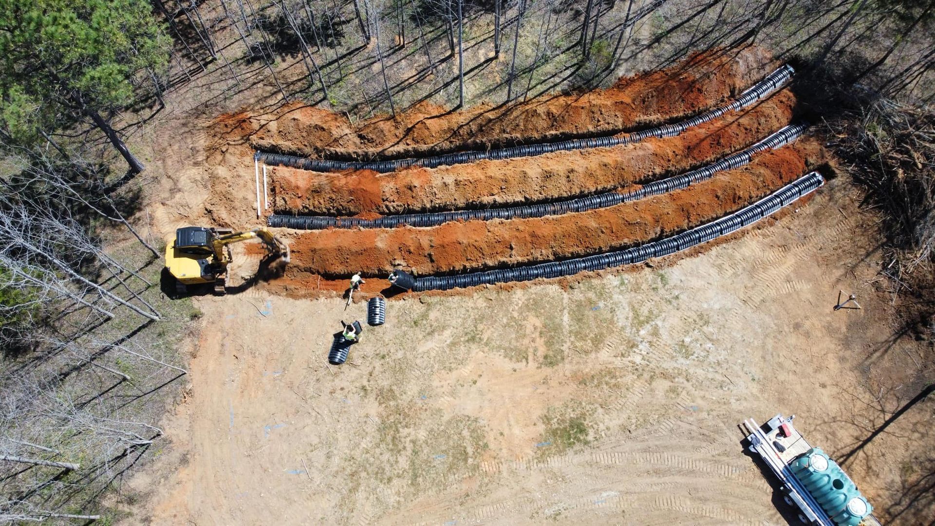 Construction site with excavator and trenches for septic system in a wooded area.