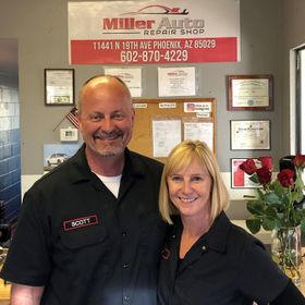 Two smiling staff members in black shirts stand in a repair shop lobby | Miller Auto Repair Shop