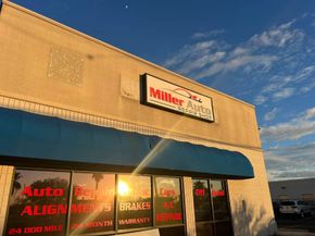 Auto repair shop storefront with blue awning and red window signs at sunset | Miller Auto Repair