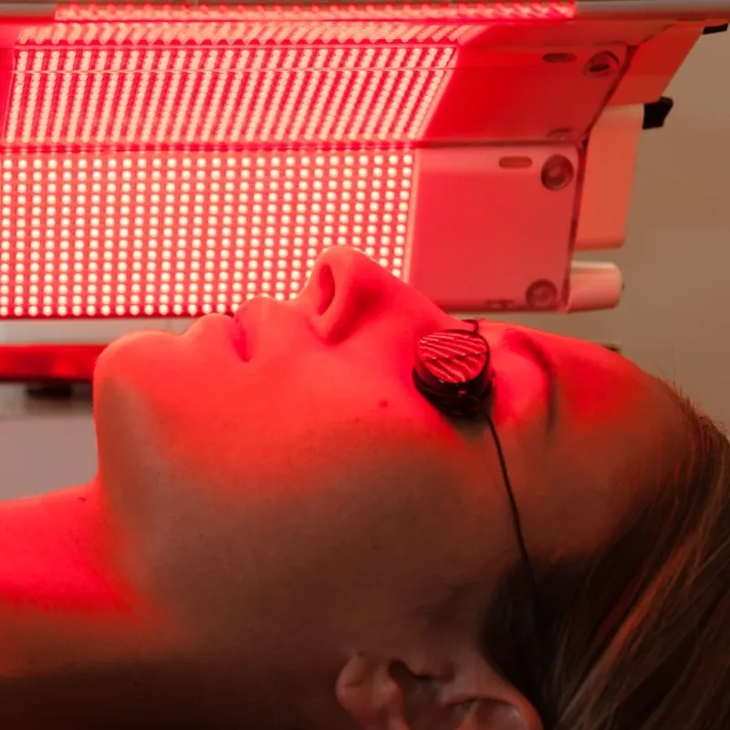 A woman is getting a red light treatment on her face.