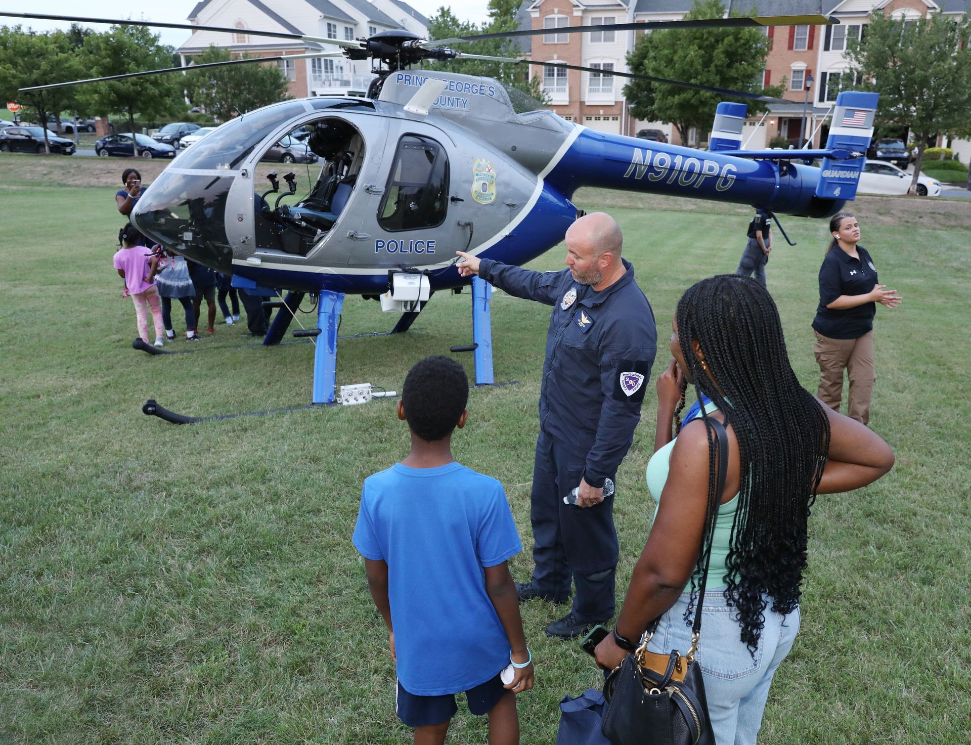 A first responder gestures toward a parked medical helicopter on a grassy field, as several people stand by and observe.