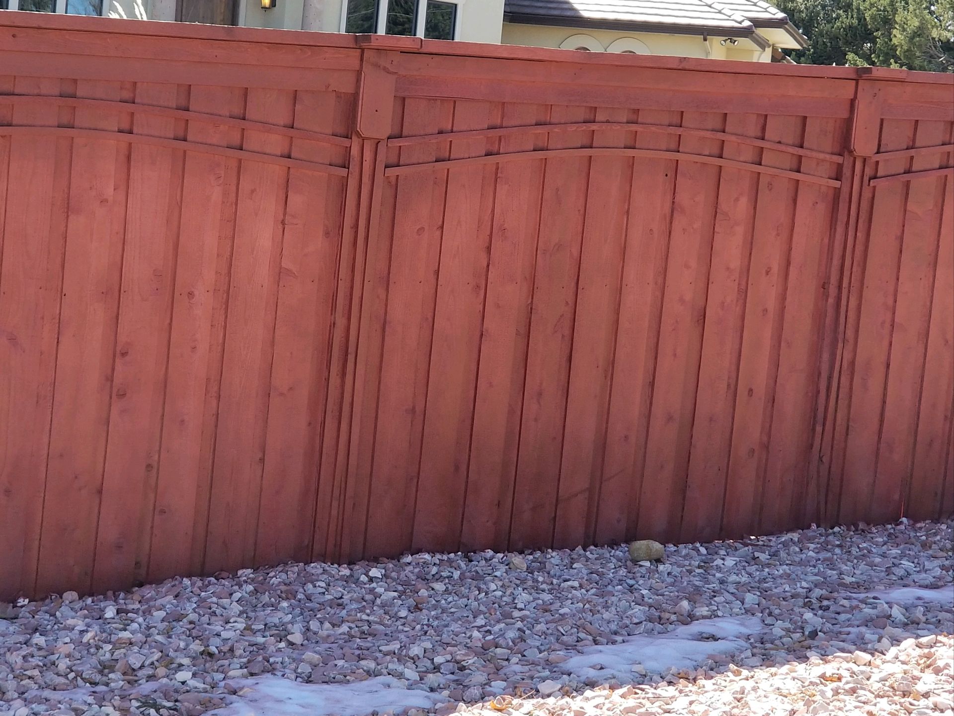 A red wooden fence is surrounded by gravel in front of a house.