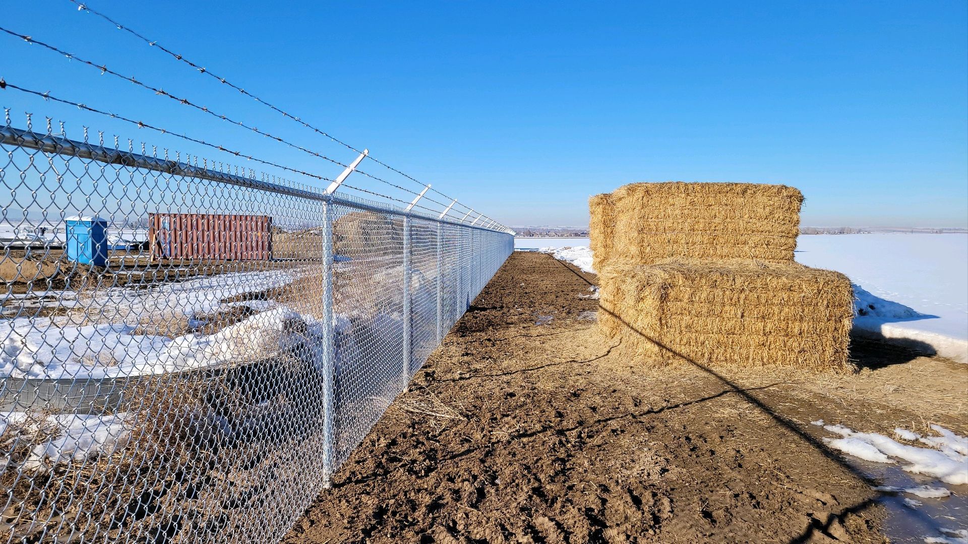 A chain link fence buit by Greater Western Fence surrounds a pile of hay bales.