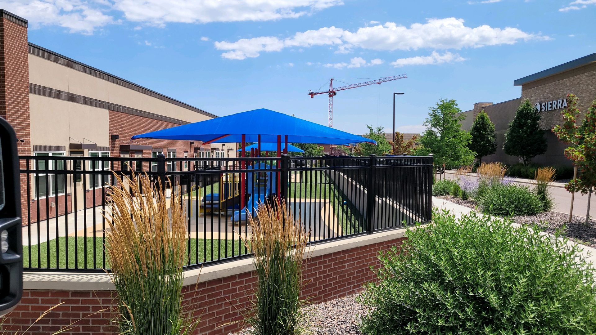 A playground with a blue umbrella over it is behind a fence built by Greater Western Fence.