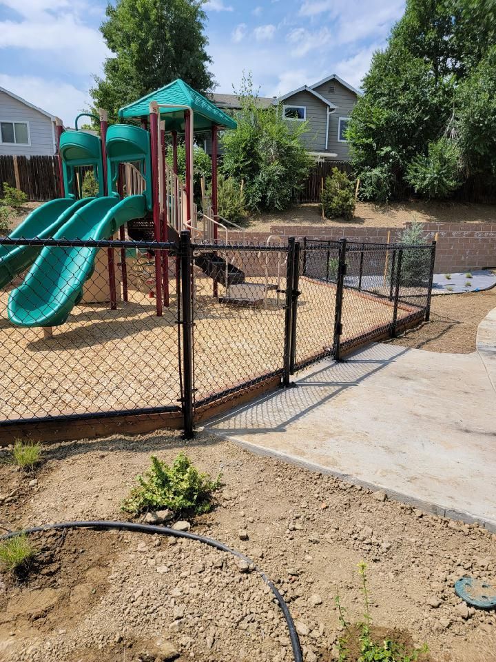 A chain link fence buit by Greater Western Fence surrounds a playground with a slide and swings.