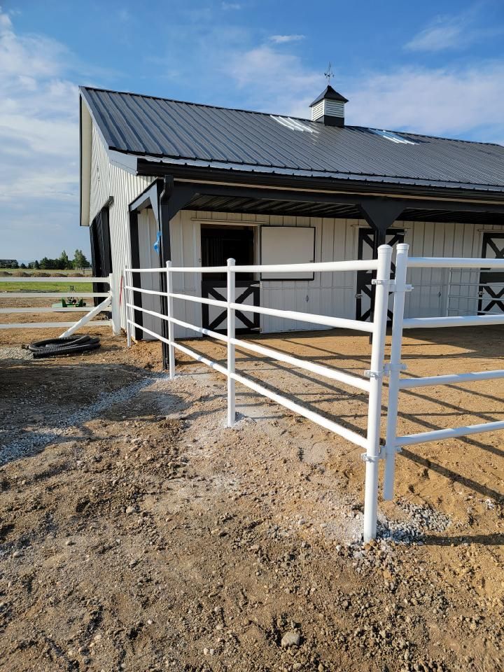 A horse barn with a white fence in front of it.