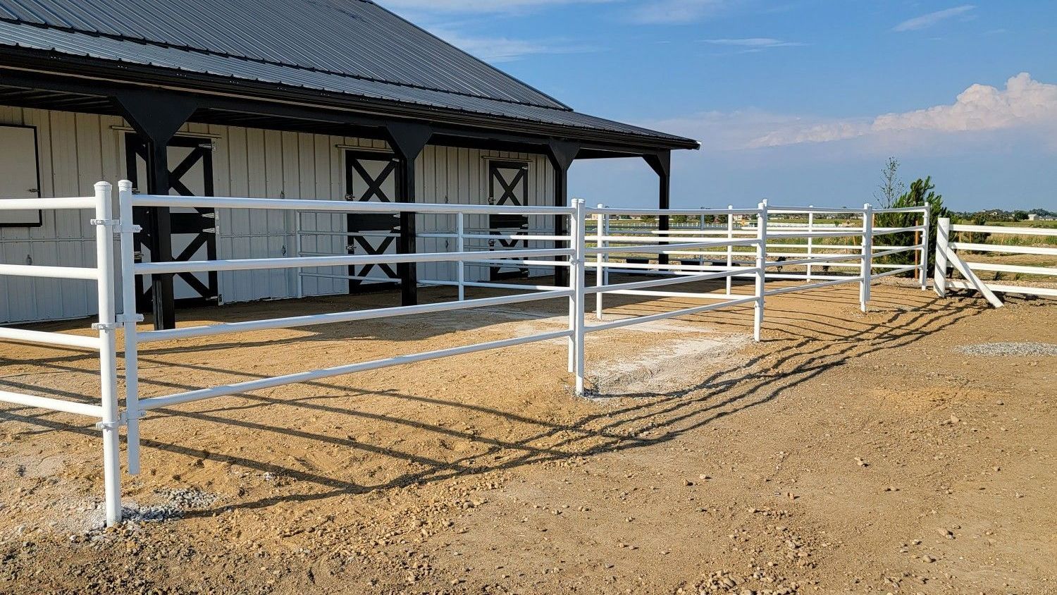 A white fence built by Greater Western Fence is in front of a white barn.