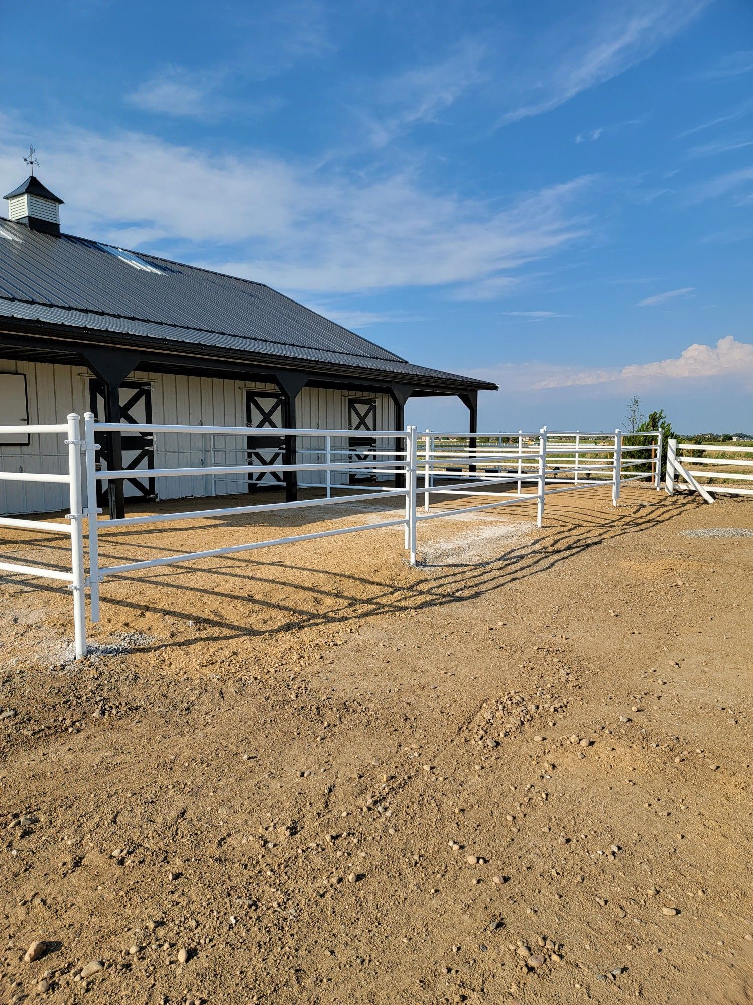 A white barn with a white fence in front of it.