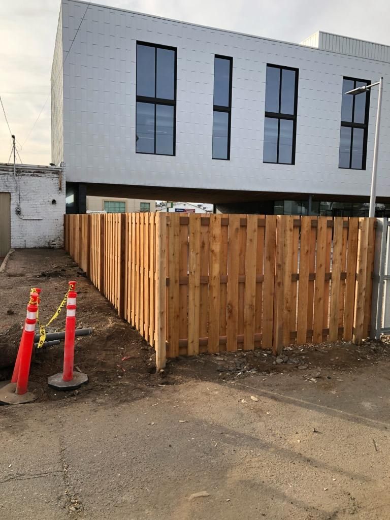 A wooden fence built by Greater Western Fence is in front of a building under construction.