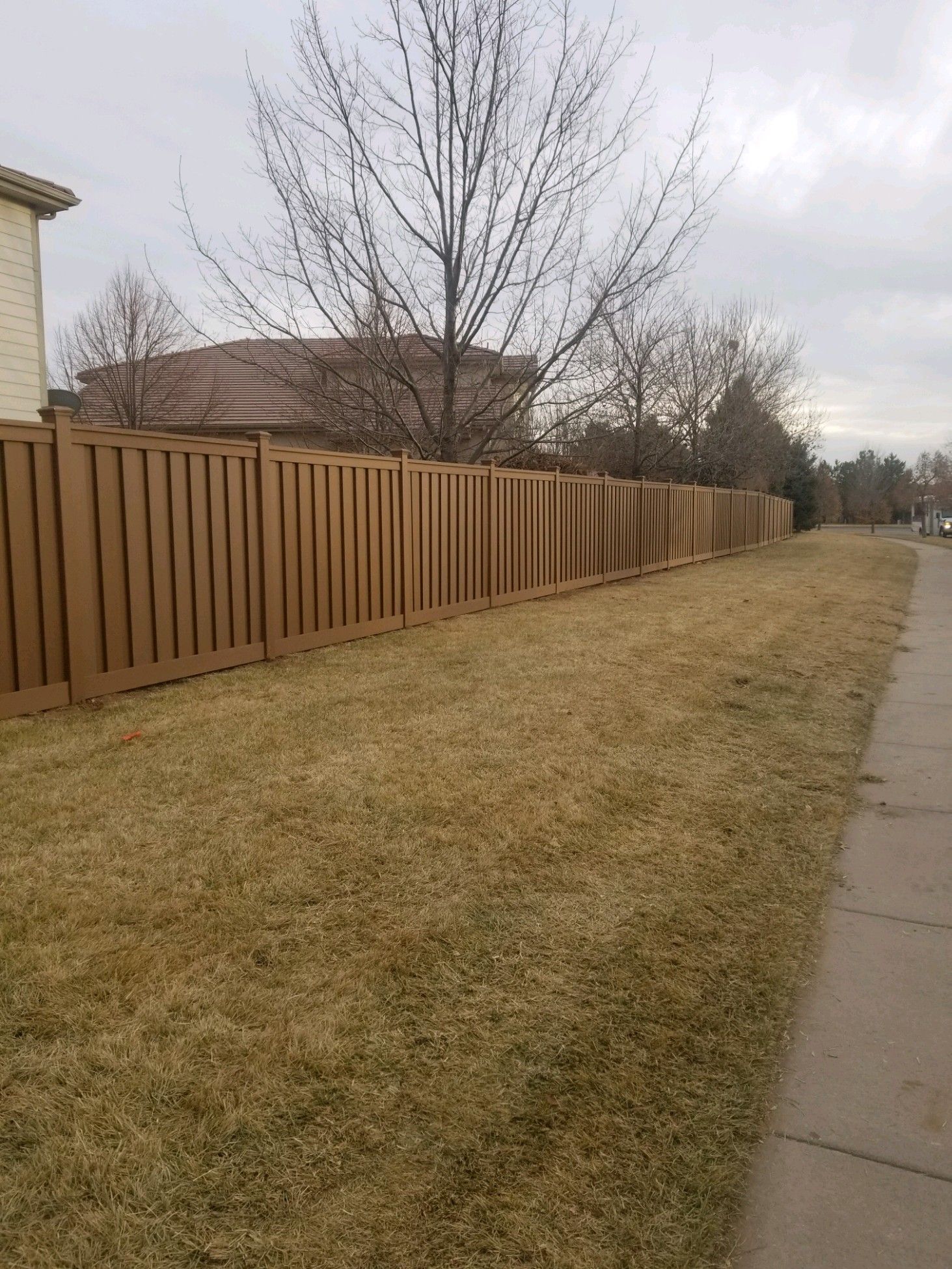 A wooden fence surrounds a grassy yard next to a sidewalk.