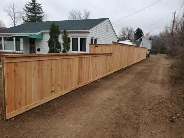 A long wooden fence along a dirt road in front of a house.