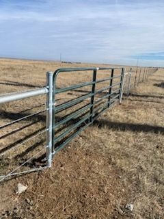 A metal livestock gate built by Greater Western Fence is sitting in the middle of a dry grass field.